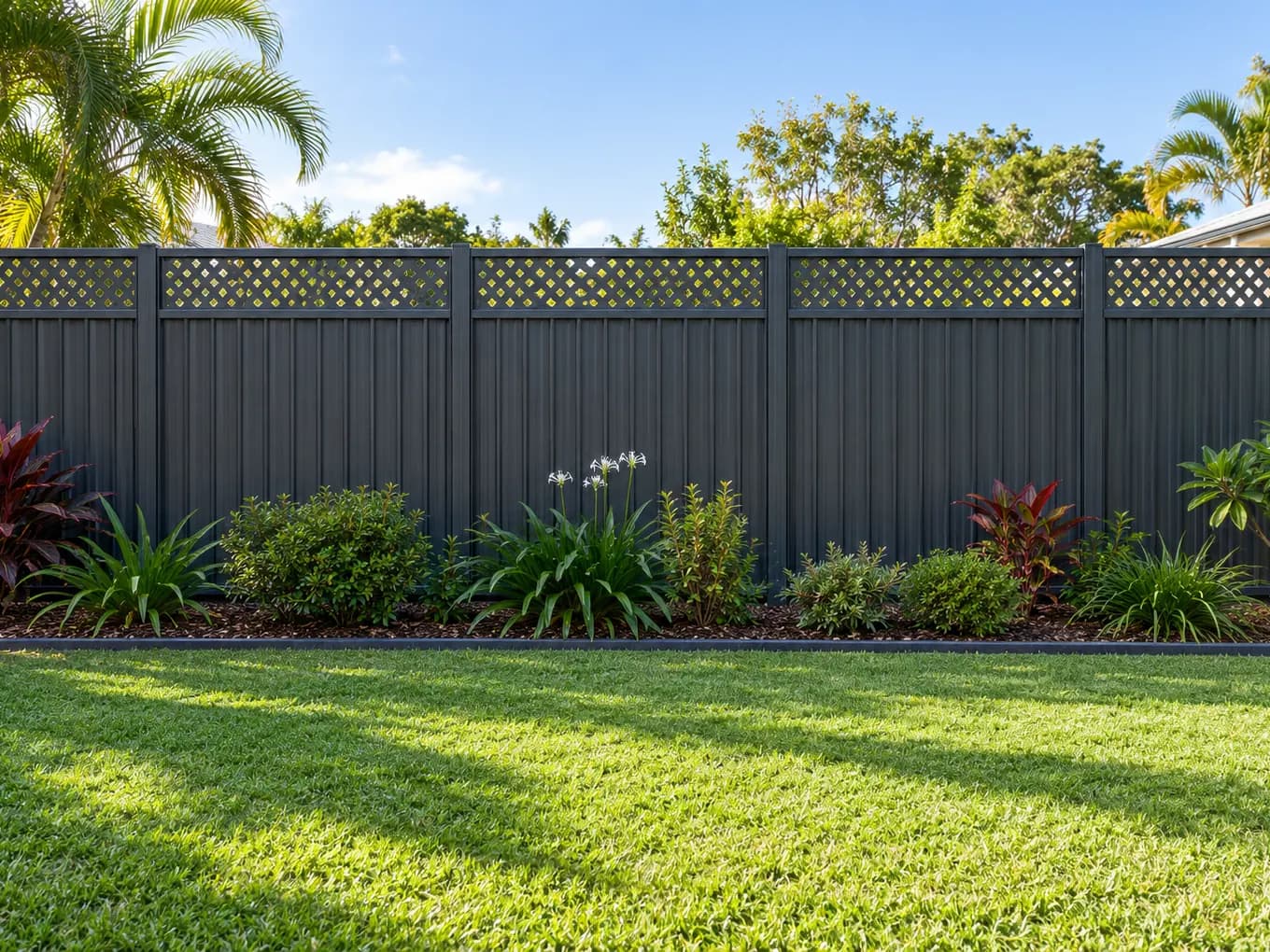 Charcoal steel panel fence with a lattice topper behind a tropical garden bed and lawn